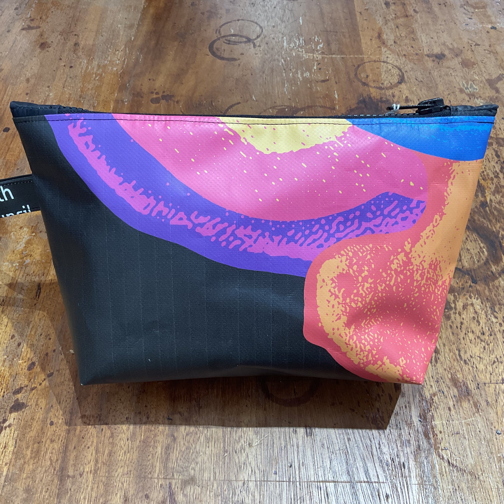 A large washbag with a multicolored geometric pattern on a black background, placed on a wooden surface.