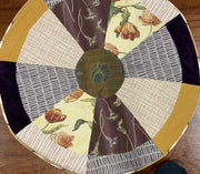 Round table with a patchwork design featuring floral and geometric patterns on a wooden floor.