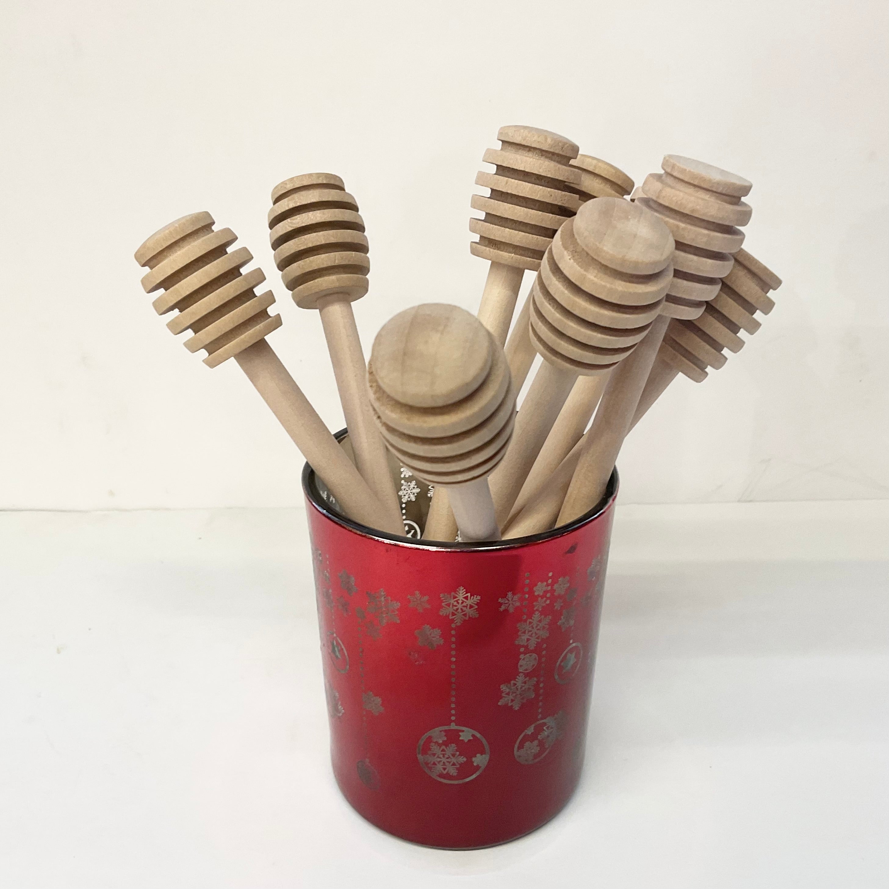 Set of wooden honey dipper sticks in a red container with silver designs on a white background