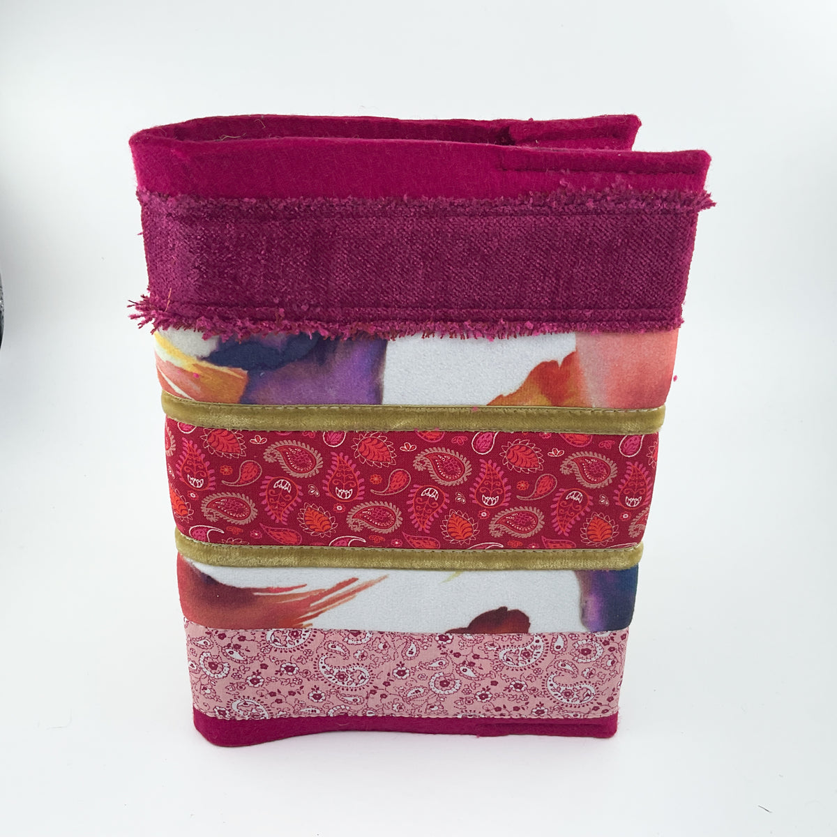 A handmade fabric tote bag featuring a layered patchwork design with a deep magenta top band, a red paisley patterned band, a white band with abstract watercolor prints, a pink paisley band, and a solid magenta bottom trim, set against a plain white background.
