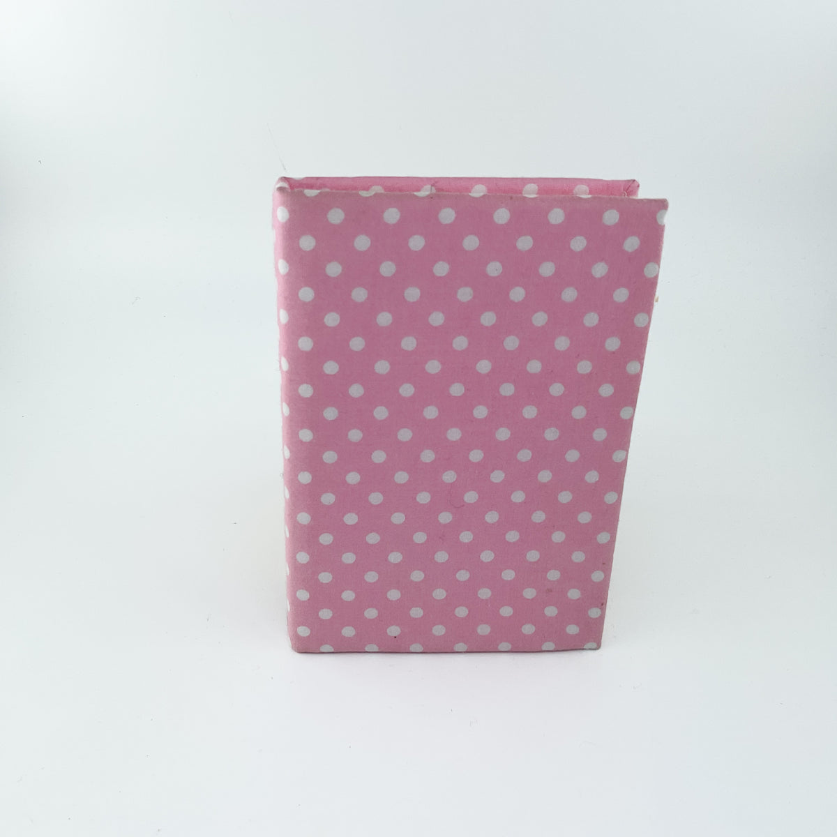 A pink notebook or journal with a white polka dot pattern, standing upright on a white background.