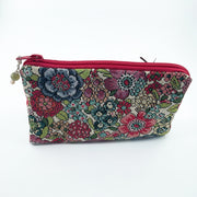 A rectangular zippered pouch with a vibrant floral tapestry pattern in red, green, blue, and beige, featuring a red zipper and a small hanging bead charm, set against a plain white background.