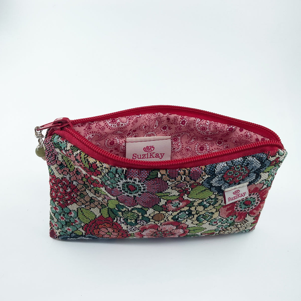 A Suzikay brand zippered pouch with a multicolor floral patterned exterior and a red interior lining, shown on a plain white background.