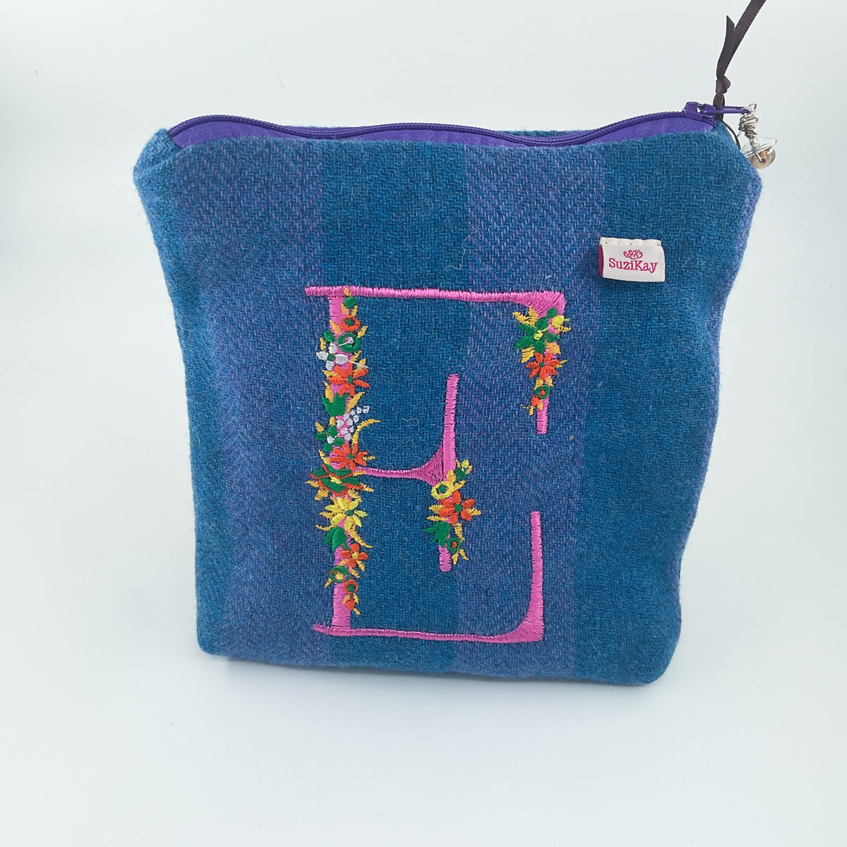 A blue herringbone woven pouch with a purple zipper, featuring a large pink embroidered letter E decorated with colorful floral embroidery, and a small RoseKay brand tag.