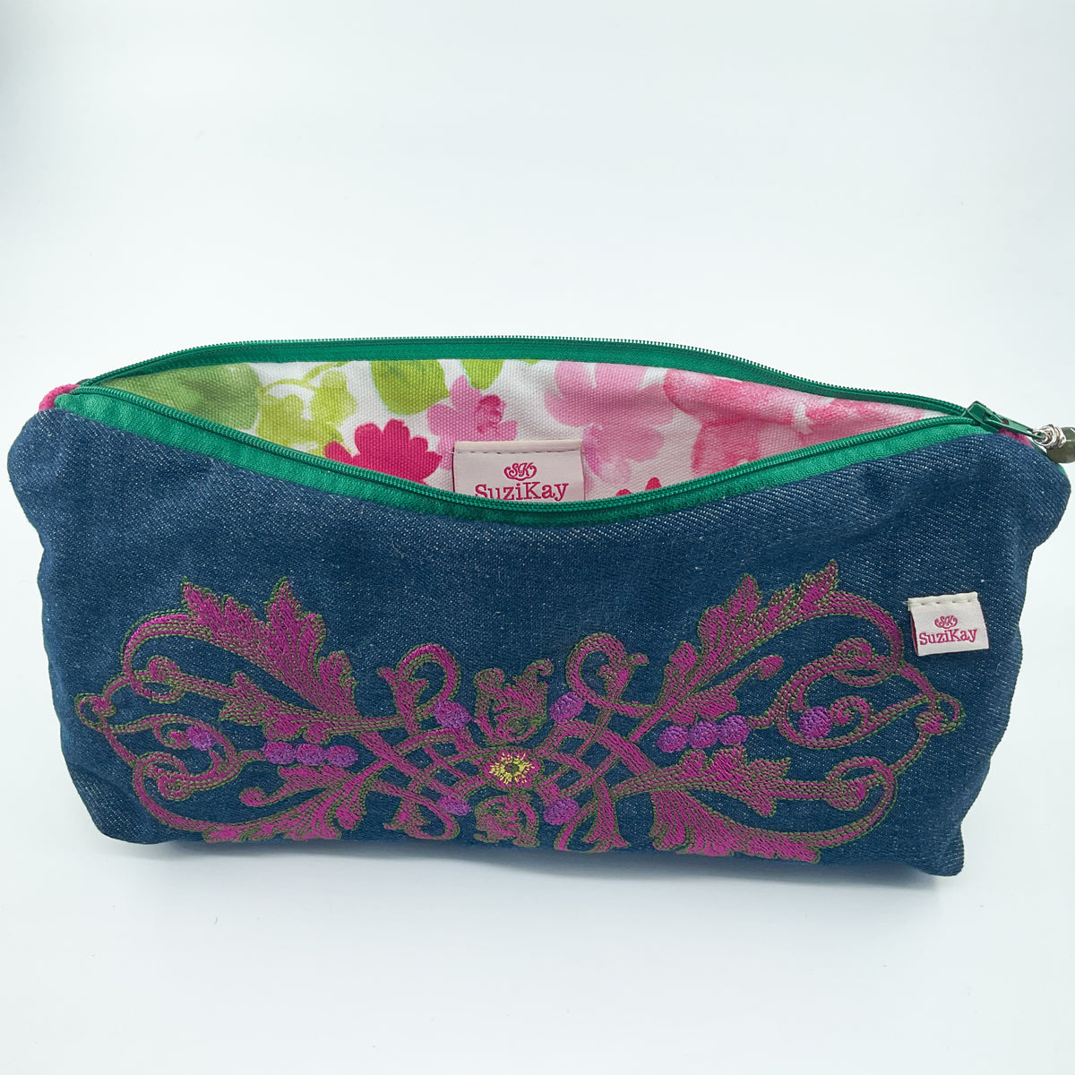 A rectangular zippered pouch in dark blue denim-like fabric with pink and green embroidered floral patterns across the front. The pouch is open, showing a pink and green floral lining, and has a small visible SwigRay brand tag.