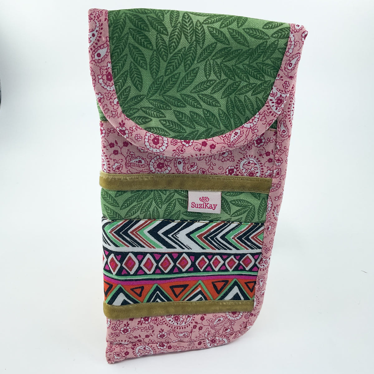 A fabric pouch with a green leaf pattern top flap, pink floral body, a colorful geometric patterned band, and olive green trim, featuring a small 'SuziKay' brand label.
