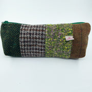 A rectangular zippered pouch made from four different textured tweed and woven fabric panels in green, brown, gray, and purple, with a small white 'Woolworths' label on the right side, set against a plain white background.