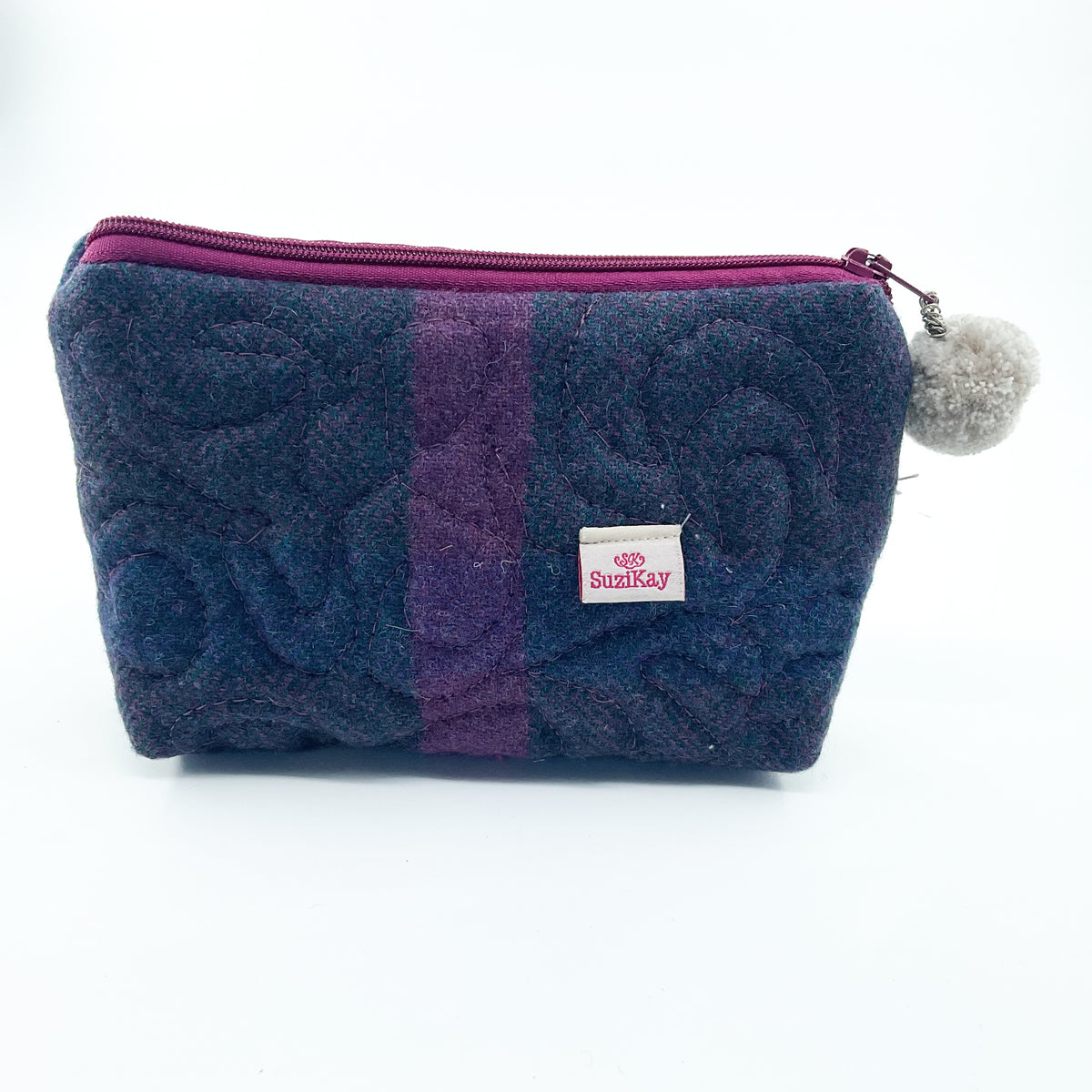 A quilted fabric zippered pouch in navy and purple with a pink zipper, a small white 'SunKay' label, and a gray pom-pom charm on a white background.