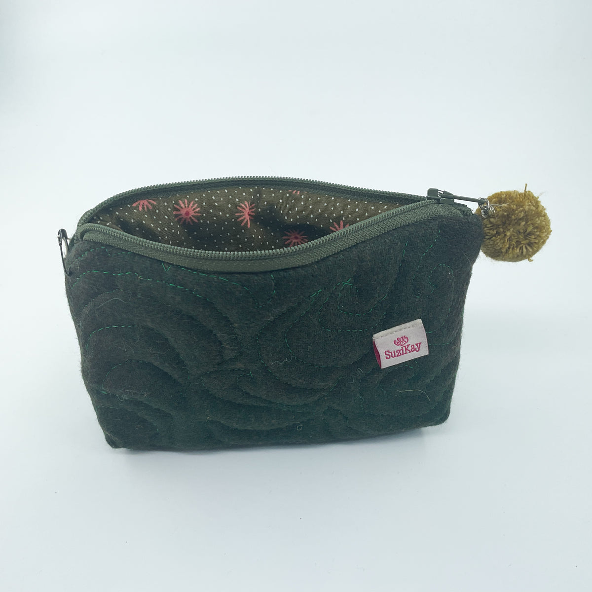 A dark green quilted fabric pouch with a zipper closure, featuring a small white 'SunBay' brand tag and a brown pom-pom charm, set against a plain white background.