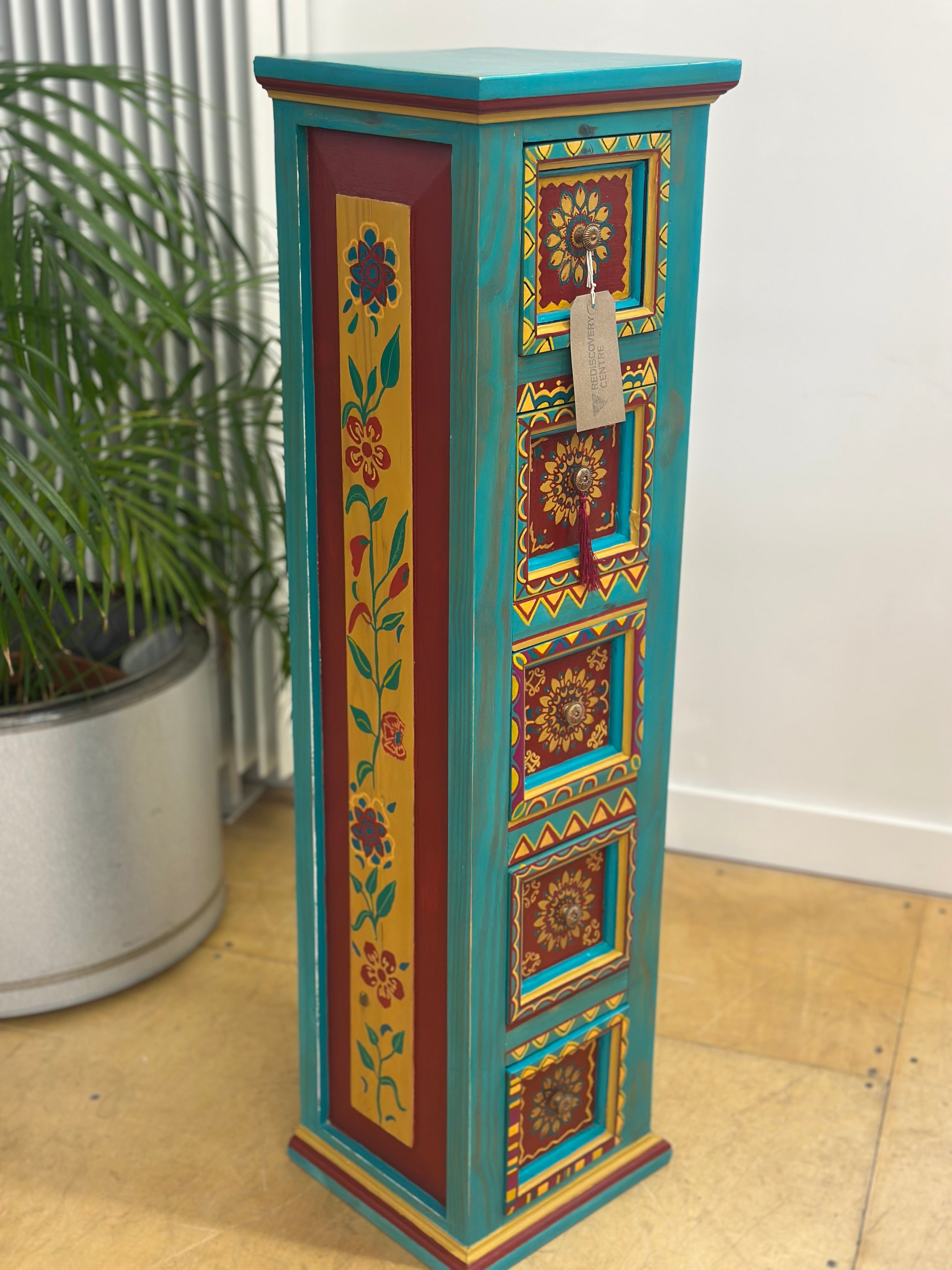 Decorative tall cabinet with floral and geometric patterns on a wooden floor.
