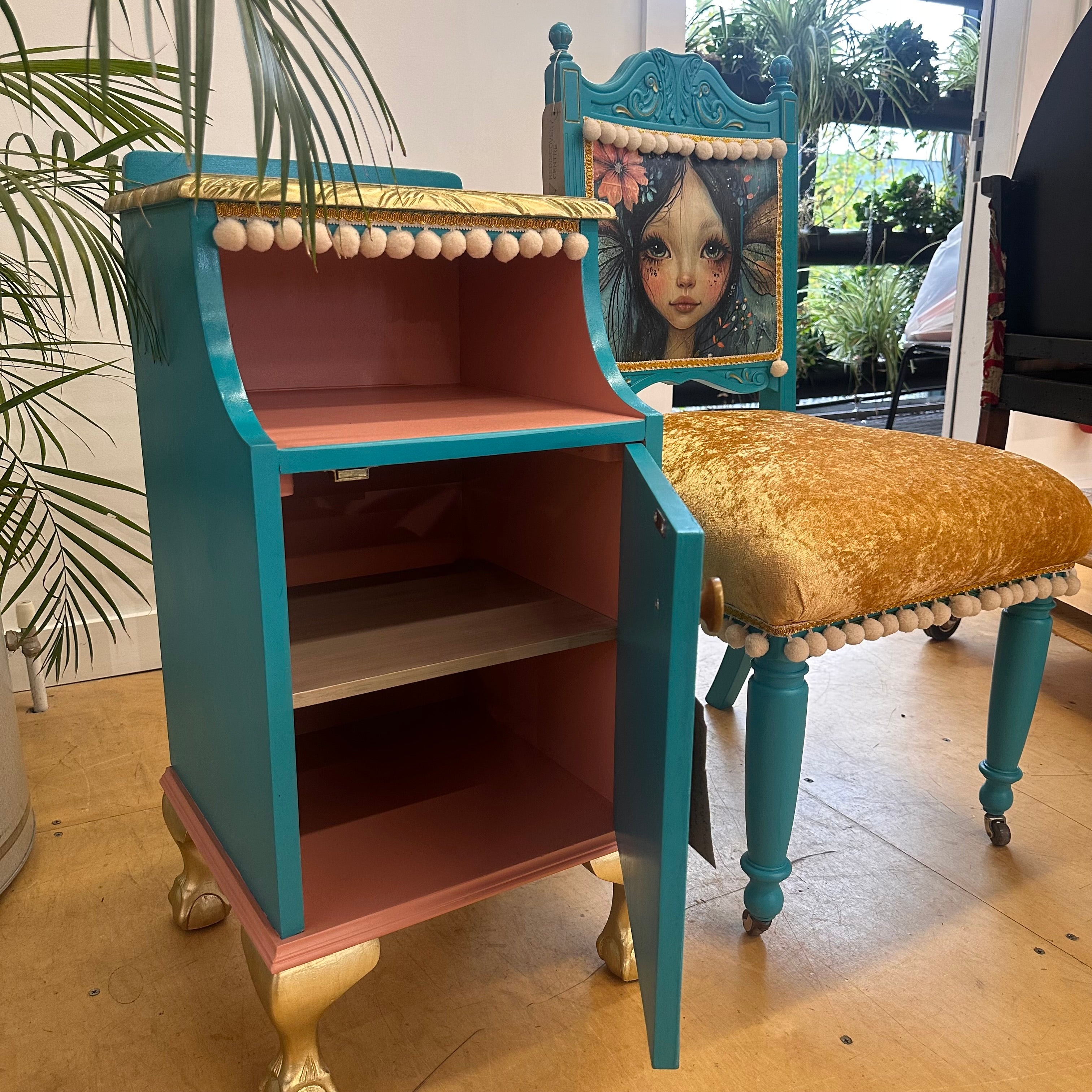 Decorative cabinet with a chair featuring a painted face in a room with plants.