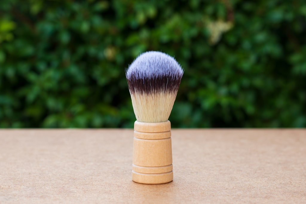Makeup brush with purple bristle head on a wooden handle against a blurred green background