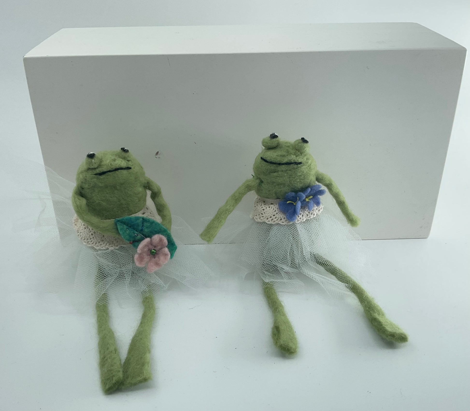 Two green frog dolls in wedding attire with flowers on a white background