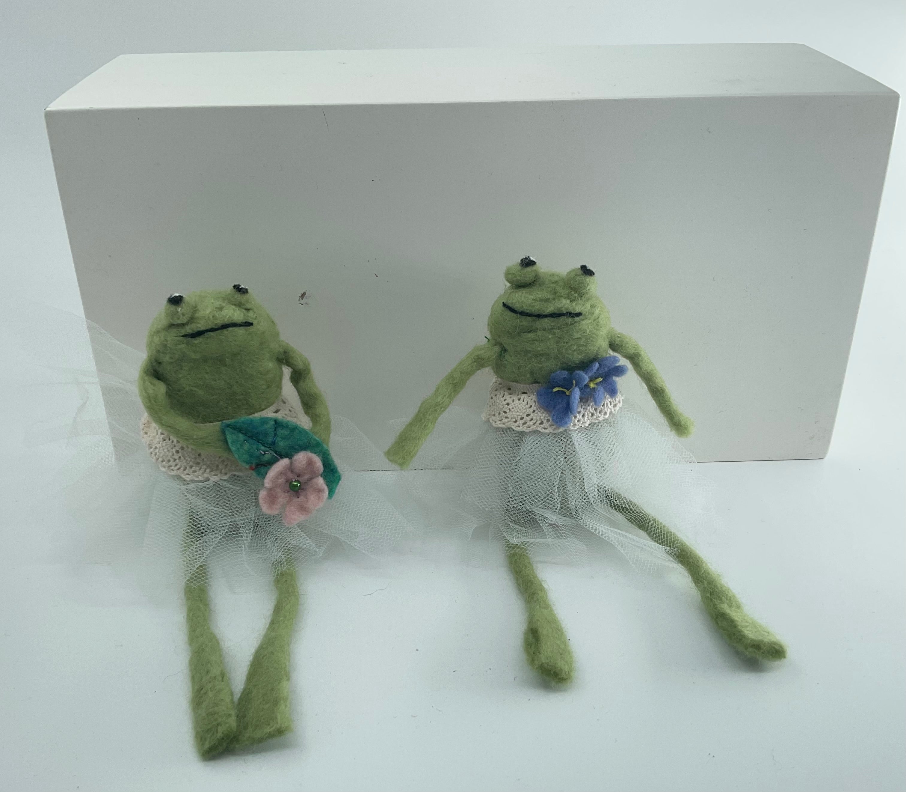 Two green frog dolls in wedding attire with flowers on a white background