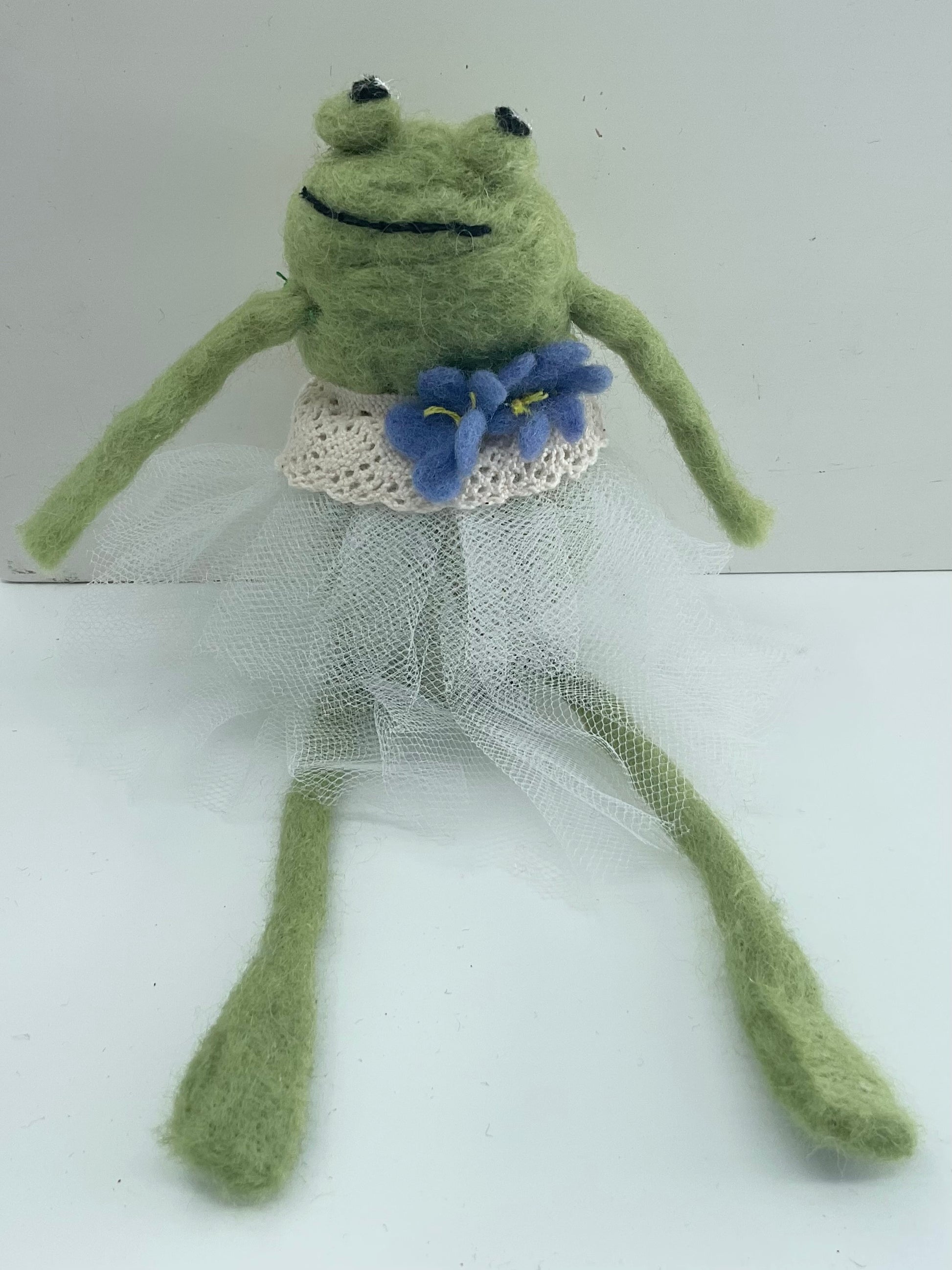 Frog toy in a white dress with a blue flower on a white background