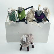 Collection of felted sheep with various accessories on a white block
