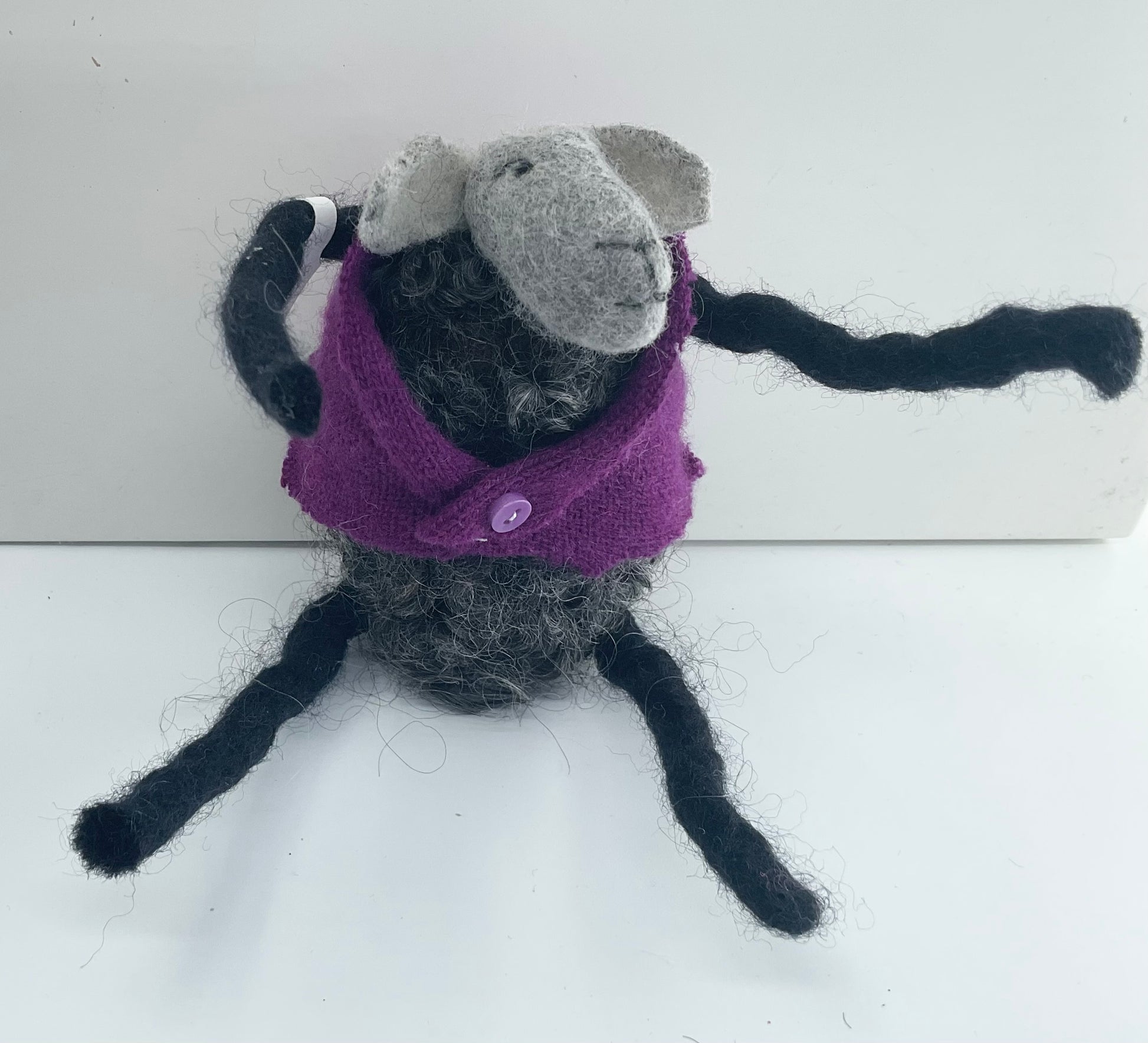 Felted sheep with a purple sweater on a white background