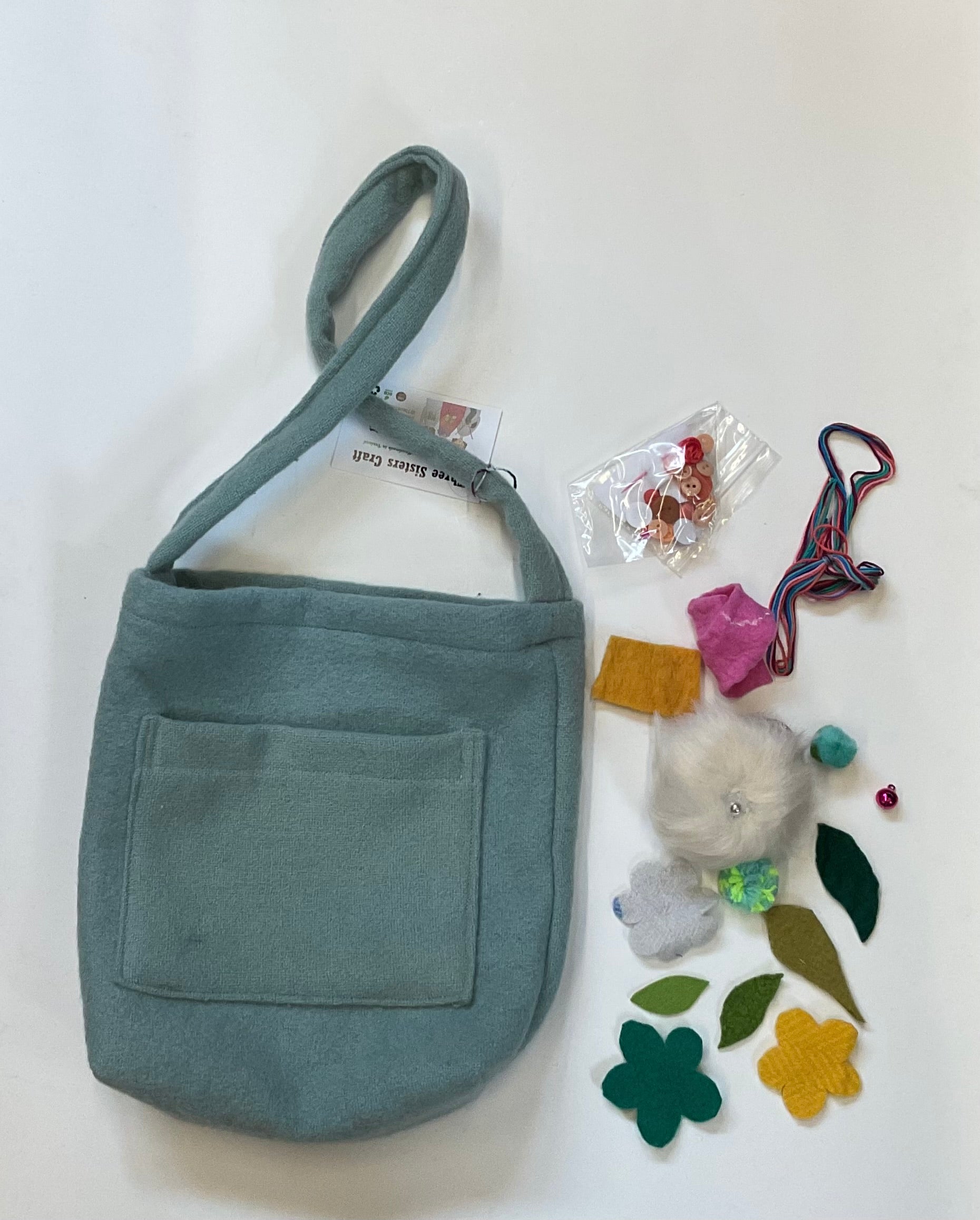 Blue fabric bag with decorative pieces of fabric, thread and buttons beside it, on a white background