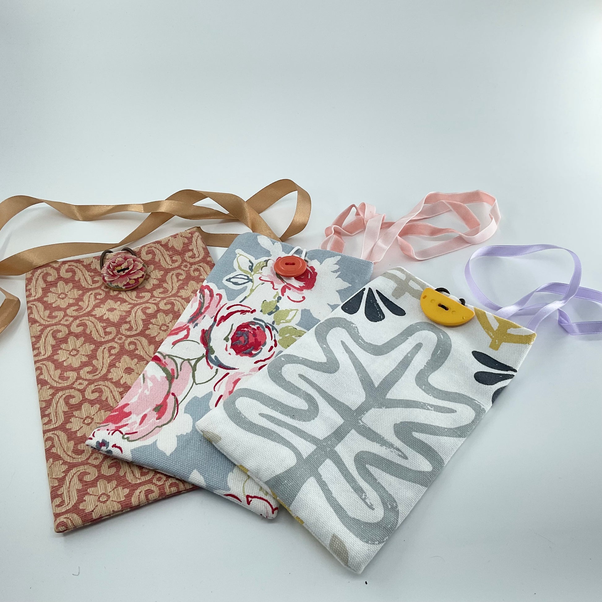 Three fabric bags with floral, floral with ribbon, and geometric designs on a white background.