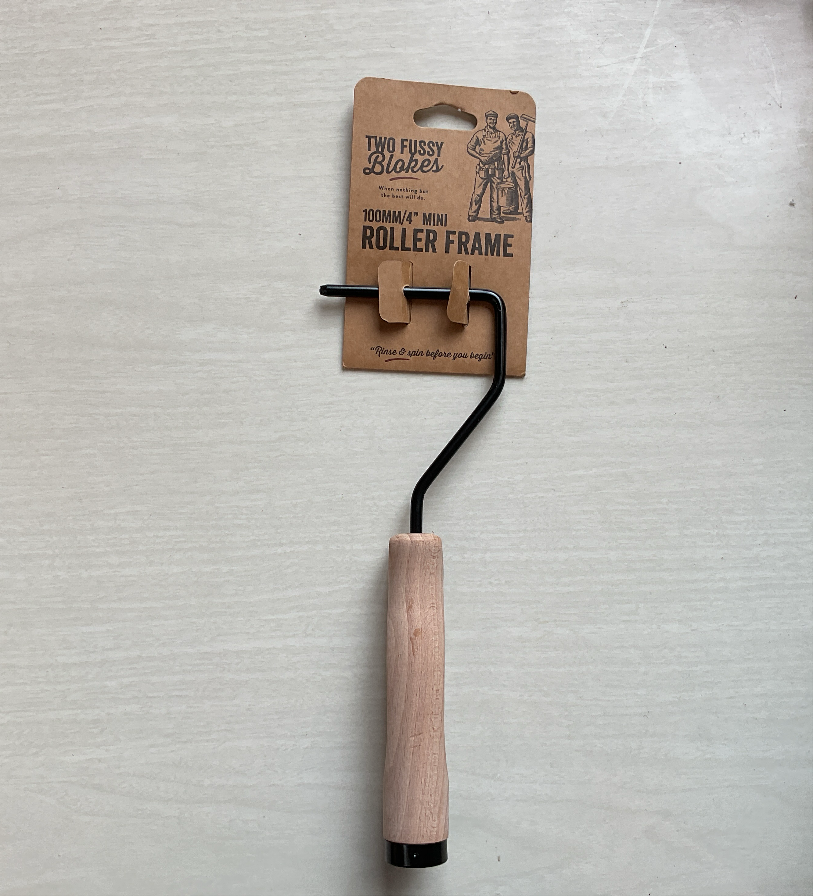 A roller frame with a wooden handle and a metal frame, laying on a flat surface with a branded cardboard packaging in the background.