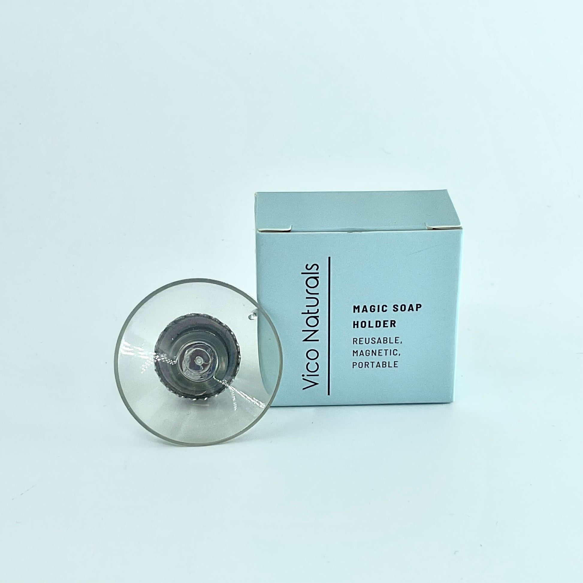 A clear, round soap holder with a magnetic base, displayed in front of its blue packaging box labeled 'Magic Soap Holder'.