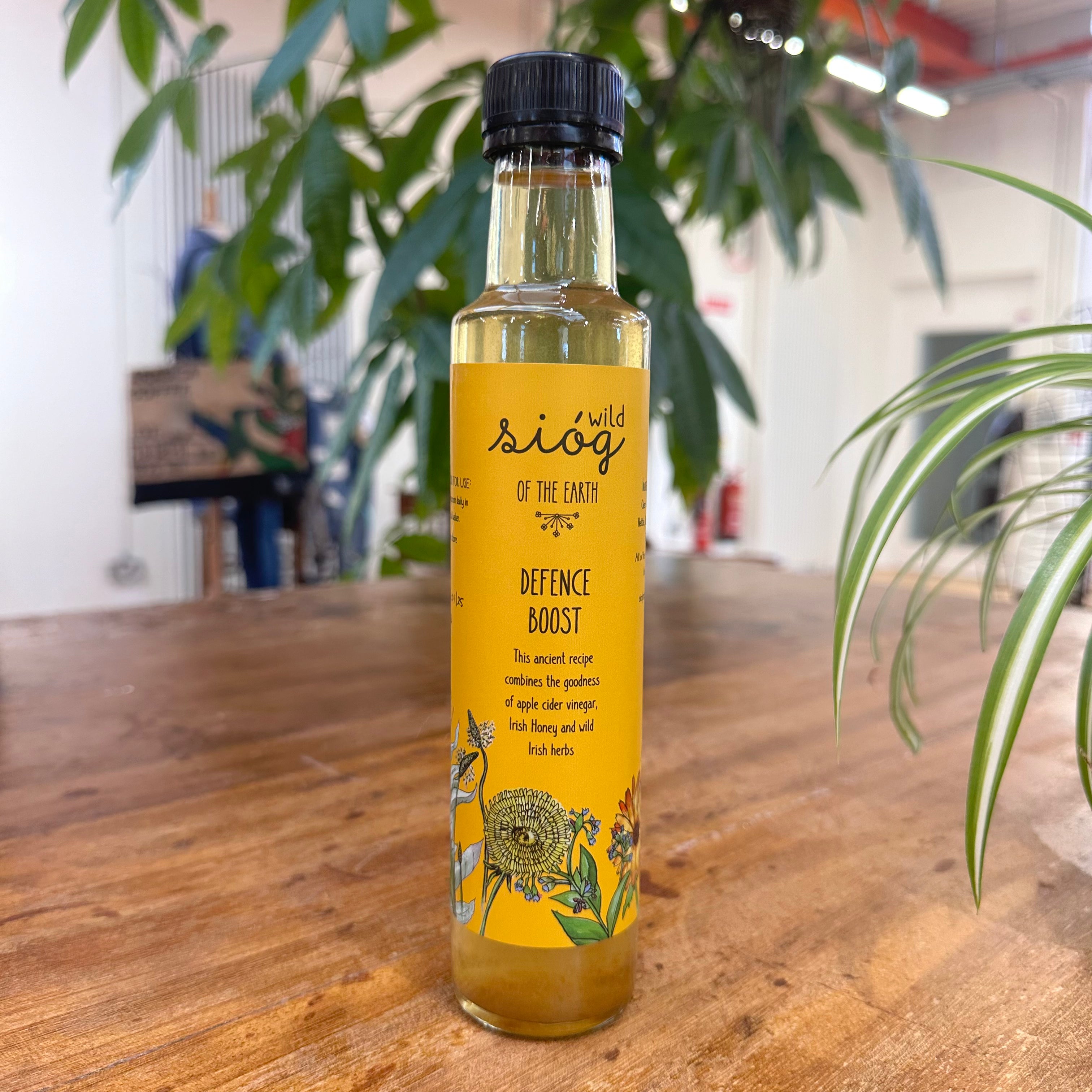 A bottle of Sióg of the Earth Defence Boost Tonic placed on a wooden table with plants in the background.