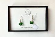 Round green glass earrings with gold hook and chain on branded white background