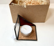 Candle in a geometric holder with a cardboard box containing straw on a white background