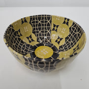 A round paper mache bowl with a yellow and black geometric pattern.