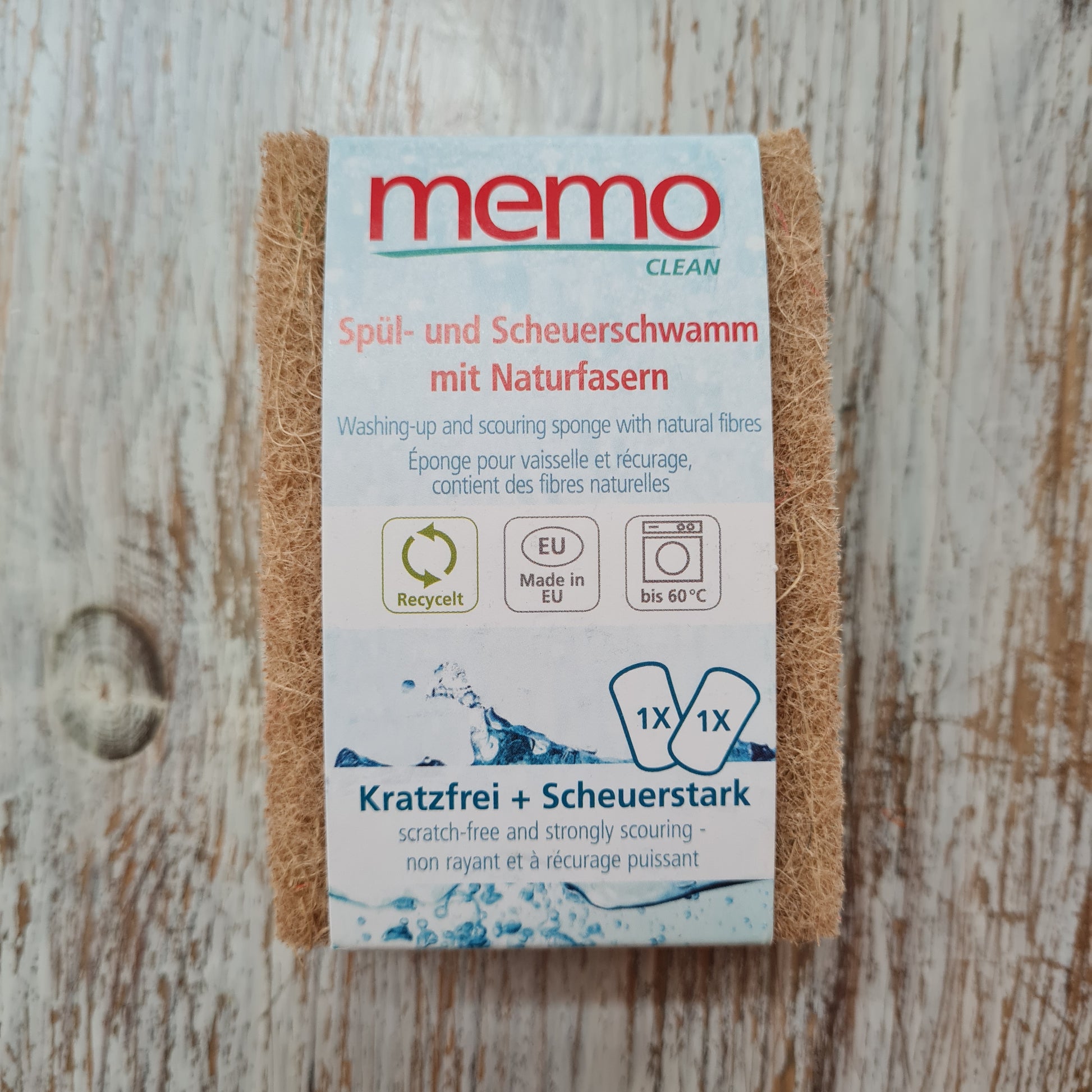 A Memo brand cleaning sponge in natural color, packaged in a cardboard box with blue and white design, highlighting its natural fibers and suitability for dishwashing and scouring.