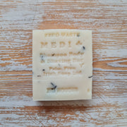 A white shampoo bar with 'MEDI' branding and various product labels including 'Shampoo Body & Shaving Bar' and 'Irish Companies Ltd'. The bar is placed on a wooden surface with visible cracks.